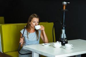 hermosa mujer de fumar un narguile y Bebiendo té en un café foto