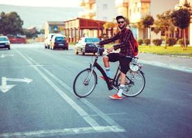 elegante hombre en Gafas de sol montando un bicicleta en ciudad calle foto