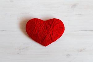 Red heart shape made from wool on white wooden background photo