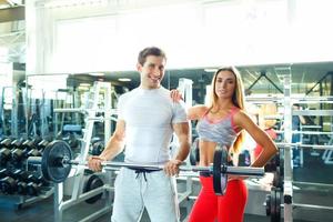 atlético hombre y mujer con barra con pesas haciendo ejercicios en el gimnasio foto