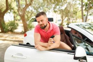 Bearded man standing near convertible with keys in hand photo