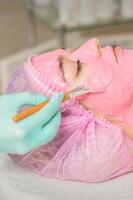 Cosmetologist applying pink alginic mask photo