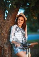 encantador joven mujer en un sombrero con un bicicleta en un parque foto