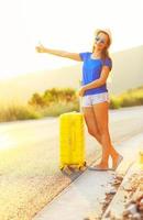 An attractive woman with a yellow suitcase is traveling on the road hitchhiking photo