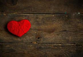 Red heart shape made from wool on old shabby wooden background photo