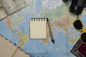 Travel Flat lay of an empty notebook, sunglasses, passport, camera over a world map