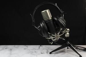 Professional microphone with black headphones over black background on white marble table photo