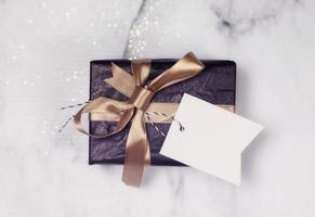 Black Gift With Gold Bow And Empty white Card on a white and black marble table with a bit of glitter photo