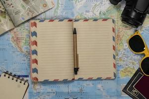 Travel Flat lay of an empty notebook, sunglasses, passport, camera over a world map photo