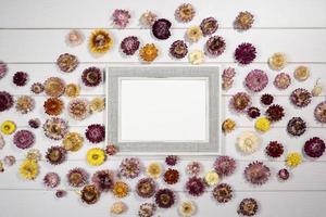 Top view of empty photo frame with dry colorful flowers over a white wooden table