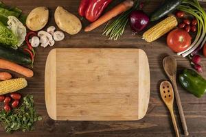 Flat lay of vegetables and food and a chopping table over a wooden table photo