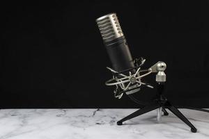 Professional microphone with black headphones over black background on white marble table photo