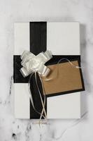 White Gift With Black Bow And Empty Card on a white and black marble table with a bit of glitter photo