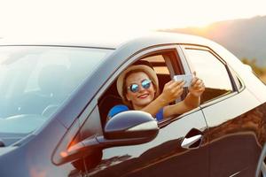 Young happy woman in hat and sunglasses making self portrait sitting in the car photo