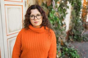 Portrait of carefree young woman smiling with urban background. Cheerful latin girl wearing eyeglasses in the city. Happy brunette woman with curly hair and spectacles smiling. photo