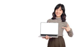 hermosa joven asiático mujer en suéter paño señalando índice dedo en ordenador portátil ordenador personal computadora y mirando a cámara con sonrisa cara y contento aislado en blanco antecedentes foto