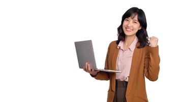hermosa joven asiático mujer en oficina ropa participación ordenador portátil ordenador personal computadora y mirando a cámara con sonrisa cara y puño arriba, aislado en blanco antecedentes foto