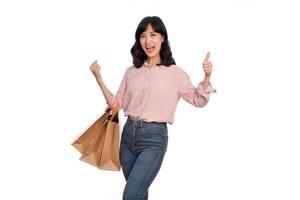 joven contento asiático mujer con casual camisa y mezclilla pantalones participación compras papel bolso aislado en blanco antecedentes foto