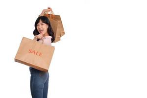 joven contento asiático mujer con casual camisa y mezclilla pantalones participación compras papel bolso aislado en blanco antecedentes foto