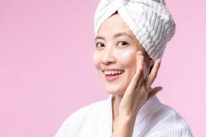 Young asian woman applying facial skincare face cream, cosmetic moisturiser on healthy natural skin make up face. Portrait glowing smile girl person model with care beauty product, spa, cosmetology. photo