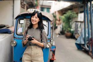 Young Asian woman backpack traveler standing a side of Tuk Tuk taxi on summer vacations at Bangkok, Thailand. photo