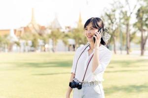 retrato hermosa joven asiático mujer con teléfono inteligente en verano fiesta vacaciones viaje con el grandioso palacio en un antecedentes a bangkok, Tailandia foto