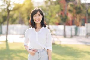 retrato joven hermosa asiático mujer con contento sonrisa alrededor al aire libre parque en soleado verano día foto