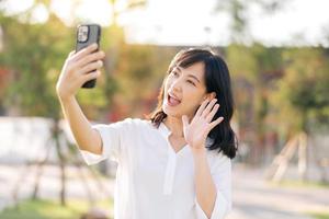 Portrait beautiful young asian woman with smart mobile phone around outdoor nature view in a sunny summer day photo