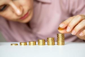 Female hand stacking gold coins into increasing columns photo