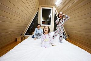 niños en suave calentar pijama jugando a de madera cabina hogar. concepto de infancia, ocio actividad, felicidad. hermano y hermanas teniendo divertido y jugando juntos. foto