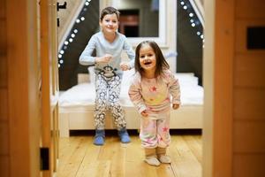 Children in soft warm pajamas playing at wooden cabin home. Concept of childhood, leisure activity, happiness. Brother and sister having fun and playing together. photo