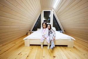 dos hermanas en suave calentar pijama jugando a de madera cabina hogar. concepto de infancia, ocio actividad, felicidad. pequeño muchachas teniendo divertido y jugando juntos. foto