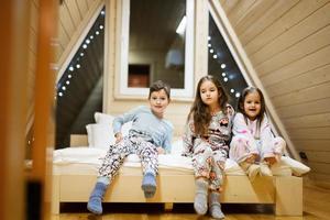 Children in soft warm pajamas playing at wooden cabin home. Concept of childhood, leisure activity, happiness. Brother and sisters having fun and playing together. photo