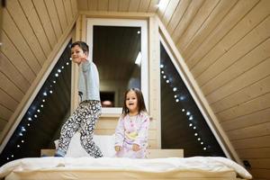 niños en suave calentar pijama jugando a de madera cabina hogar. concepto de infancia, ocio actividad, felicidad. hermano y hermana teniendo divertido y jugando juntos. foto