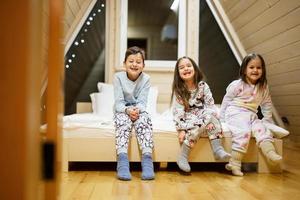 Children in soft warm pajamas playing at wooden cabin home. Concept of childhood, leisure activity, happiness. Brother and sisters having fun and playing together. photo