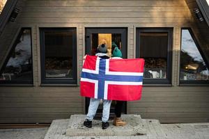 Back of couple outside cabin house holding Norway flag. Scandinavian culture, norwegian people. photo