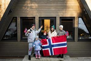 Portrait of family with kids outside cabin house holding Norway flags. Scandinavian culture, norwegian people. photo