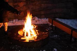 chico calentar su manos por el fuego pozo en invierno noche. foto