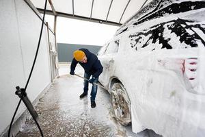 hombre lavando un camión suv americano con un trapeador en un lavado de autoservicio en clima frío. foto