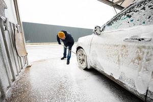 Man washing american SUV car with mop at a self service wash in cold weather. photo