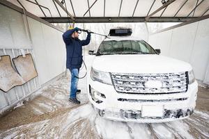 hombre lavando agua a alta presión coche suv americano con portaequipajes en autoservicio de lavado en clima frío. foto