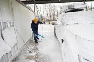 hombre lavando un automóvil suv americano con portaequipajes en un lavado de autoservicio en clima frío. foto