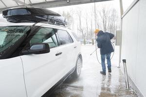 hombre lavando agua a alta presión coche suv americano con portaequipajes en autoservicio de lavado en clima frío. foto