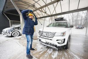 hombre lavando agua a alta presión coche suv americano con portaequipajes en autoservicio de lavado en clima frío. foto