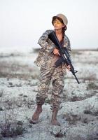 hembra soldado vestido en un camuflaje con un pistola en el al aire libre foto