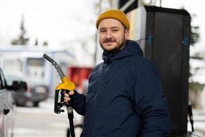 Man hold fuel pump while refueling his car at the gas station in cold weather. photo