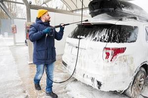 hombre lavando un automóvil suv americano con portaequipajes en un lavado de autoservicio en clima frío. foto