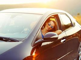 sonriente mujer conducción un coche a puesta de sol foto