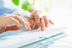 Woman office worker with pen in hand typing on the keyboard photo