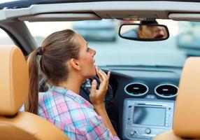 Woman corrects makeup looking in the rearview mirror in a convertible photo